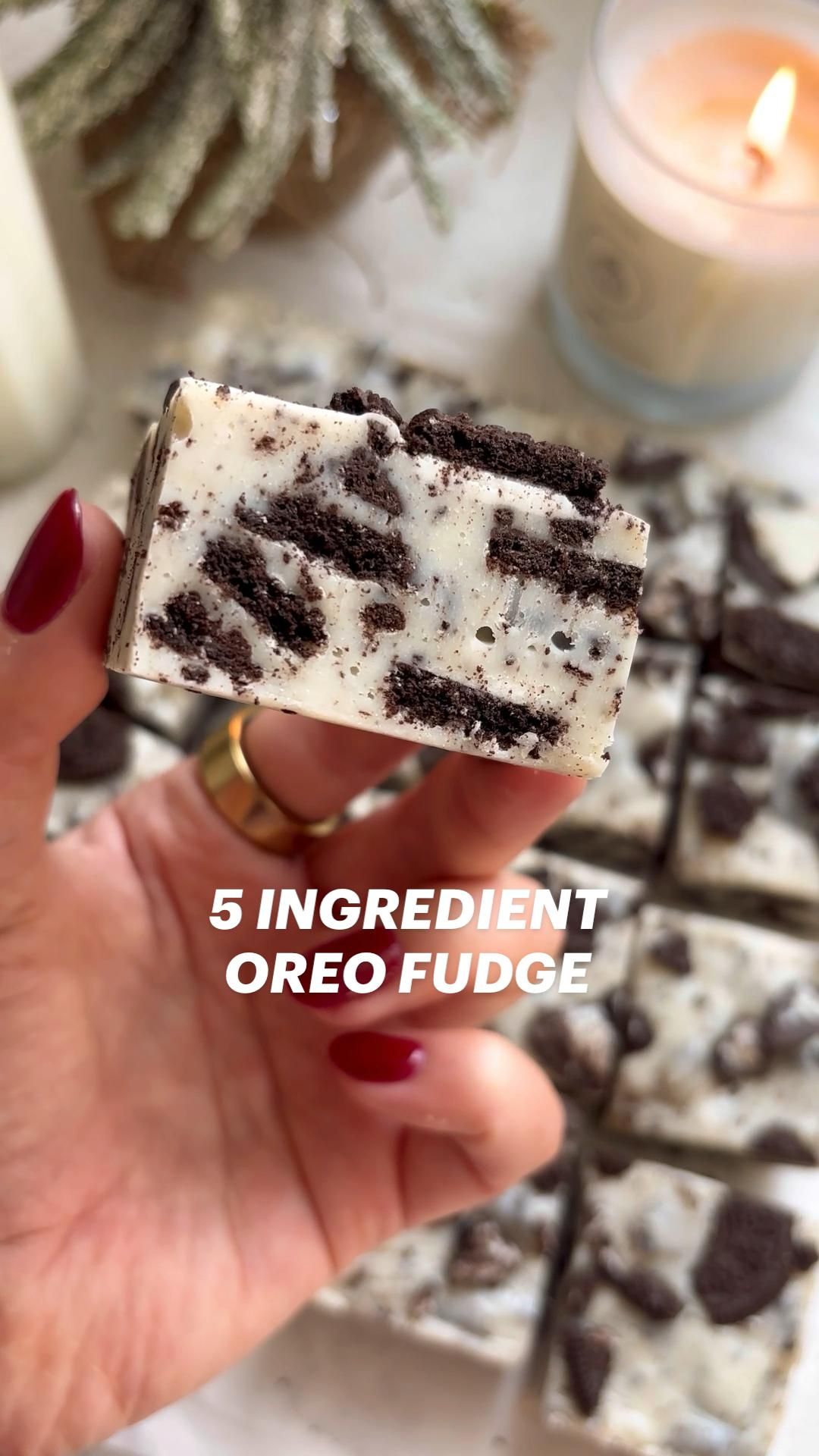 Hand holding a square of white fudge studded with crushed dark sandwich cookies.