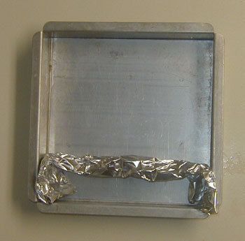 Aluminum foil crumpled into a divider inside a square aluminum baking pan.