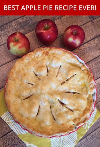 Baked apple pie with a golden-brown top crust and three red apples next to it on a wooden surface