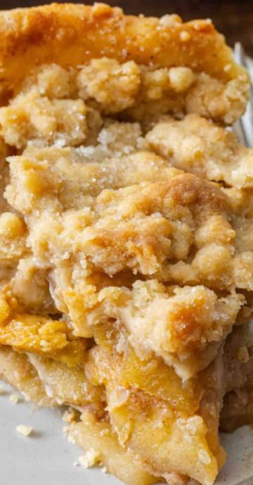 Close-up of a slice of Dutch apple pie with a golden, sugary crumb topping and visible apple filling.