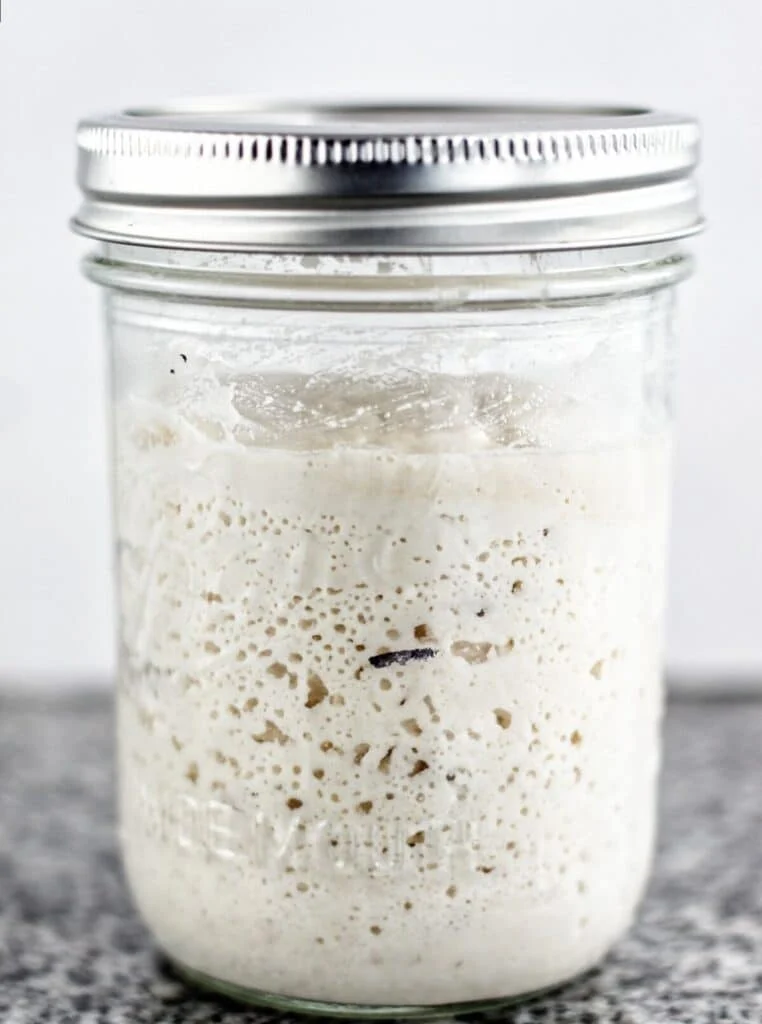Active sourdough starter in a glass jar with bubbles on the surface