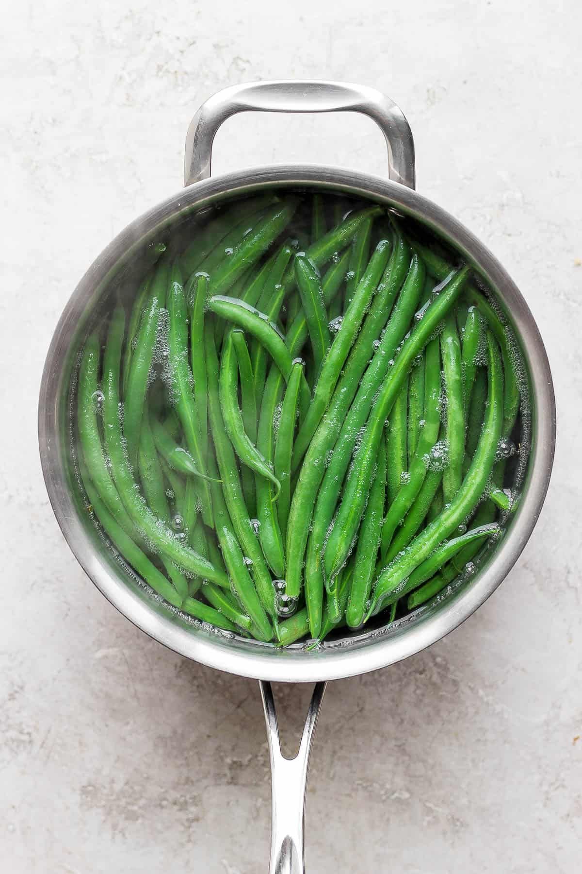 Close-up of fresh green beans submerged in a pot of gently boiling water on a stove.