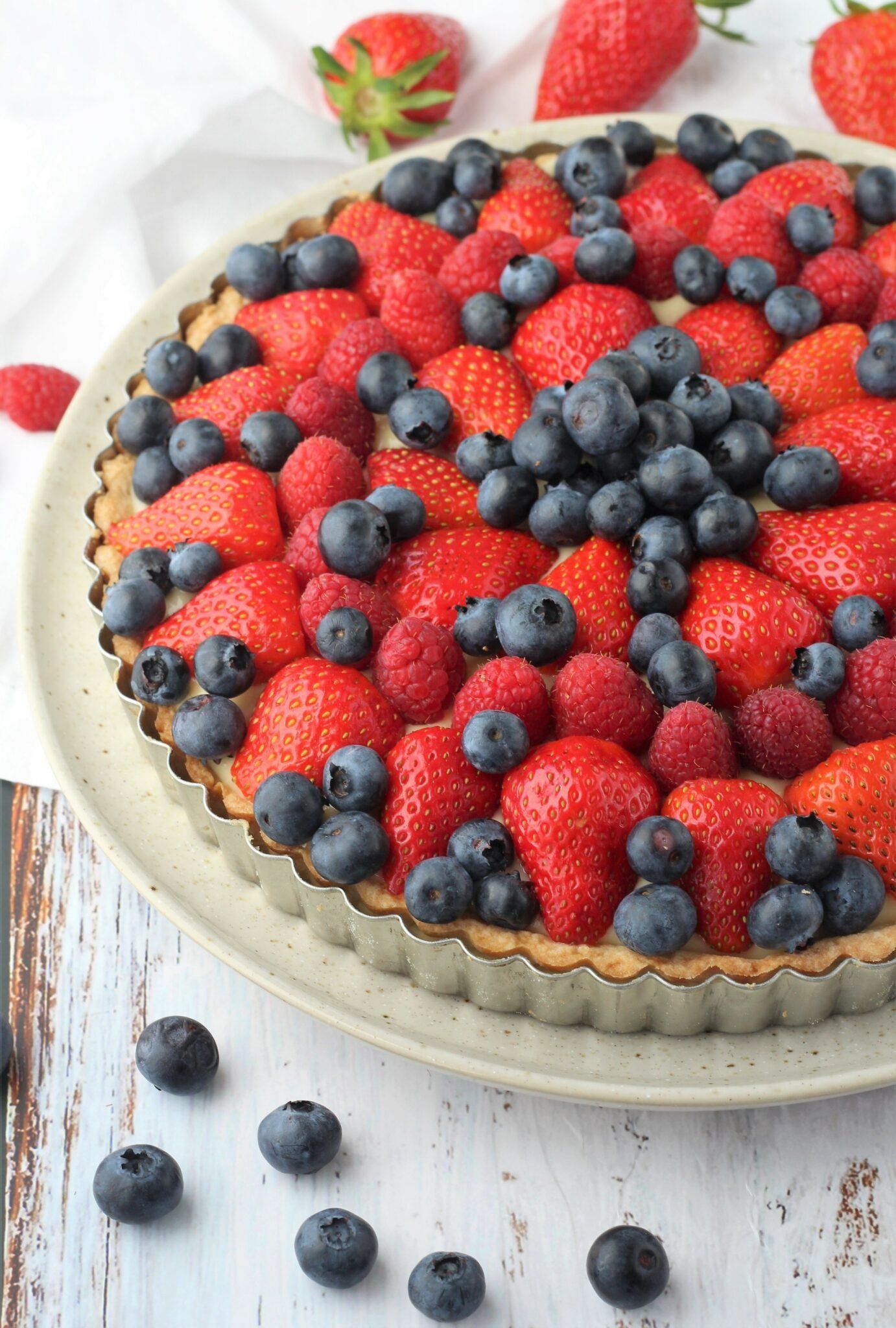 Close-up of a fruit tart with strawberries, blueberries, and raspberries over pastry cream in a fluted tart pan.